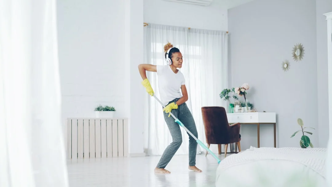 An adult woman in red coveralls operates a vacuum cleaner in a modern indoor setting, focusing on cleaning tasks.